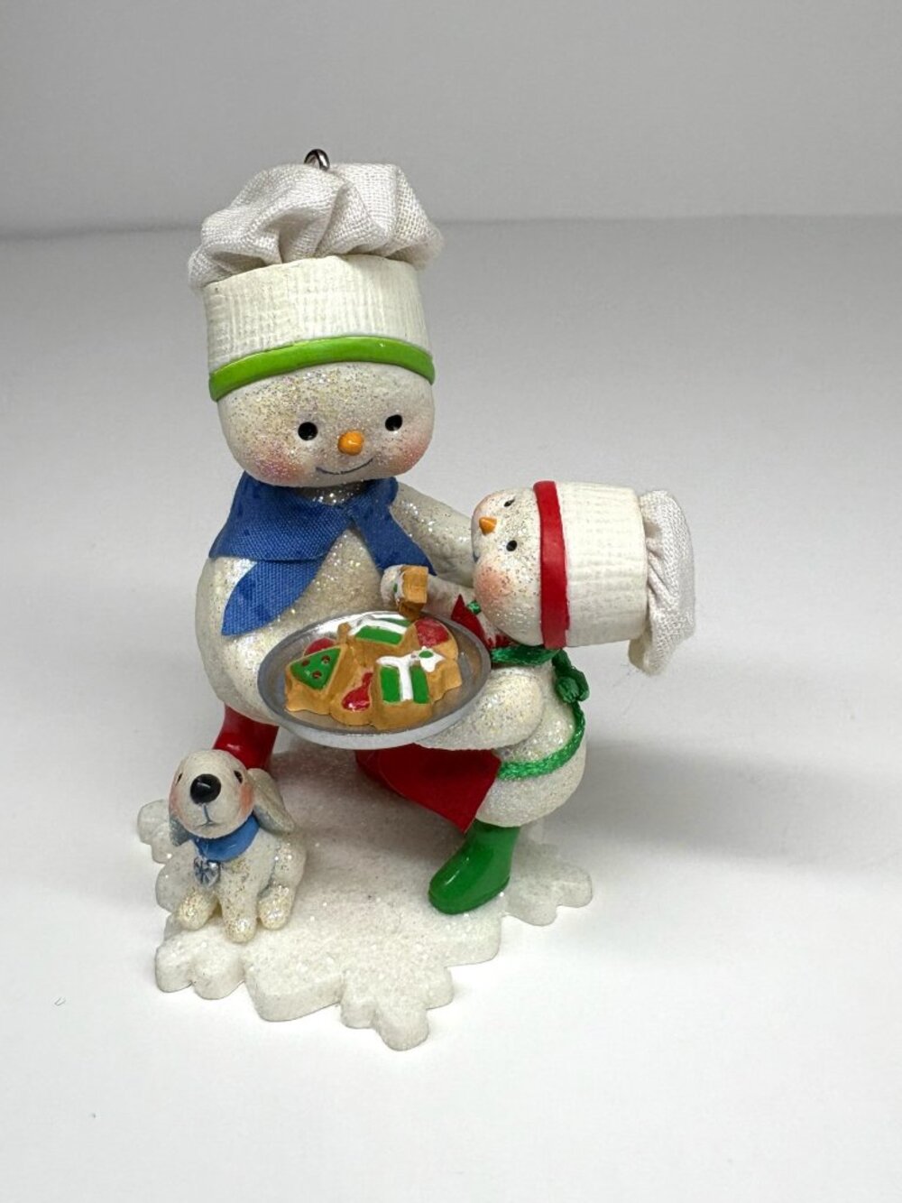 Features a larger snowman and a smaller snowman wearing chef hats and holding a